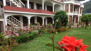 A large, white building with multiple balconies and a red roof, surrounded by well-maintained gardens and potted plants. - Hotel Akbar  (Srinagar)