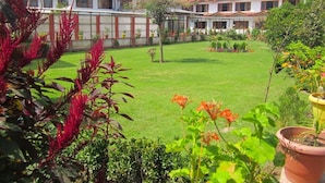 A courtyard with a lawn, potted plants, and a row of buildings with red roofs. - Hotel Akbar  (Srinagar)