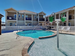 A swimming pool with a white fence and lounge chairs, surrounded by multi-story buildings with balconies. - Catalina Island by Silver Sands Vacation Rentals (Corpus Christi)