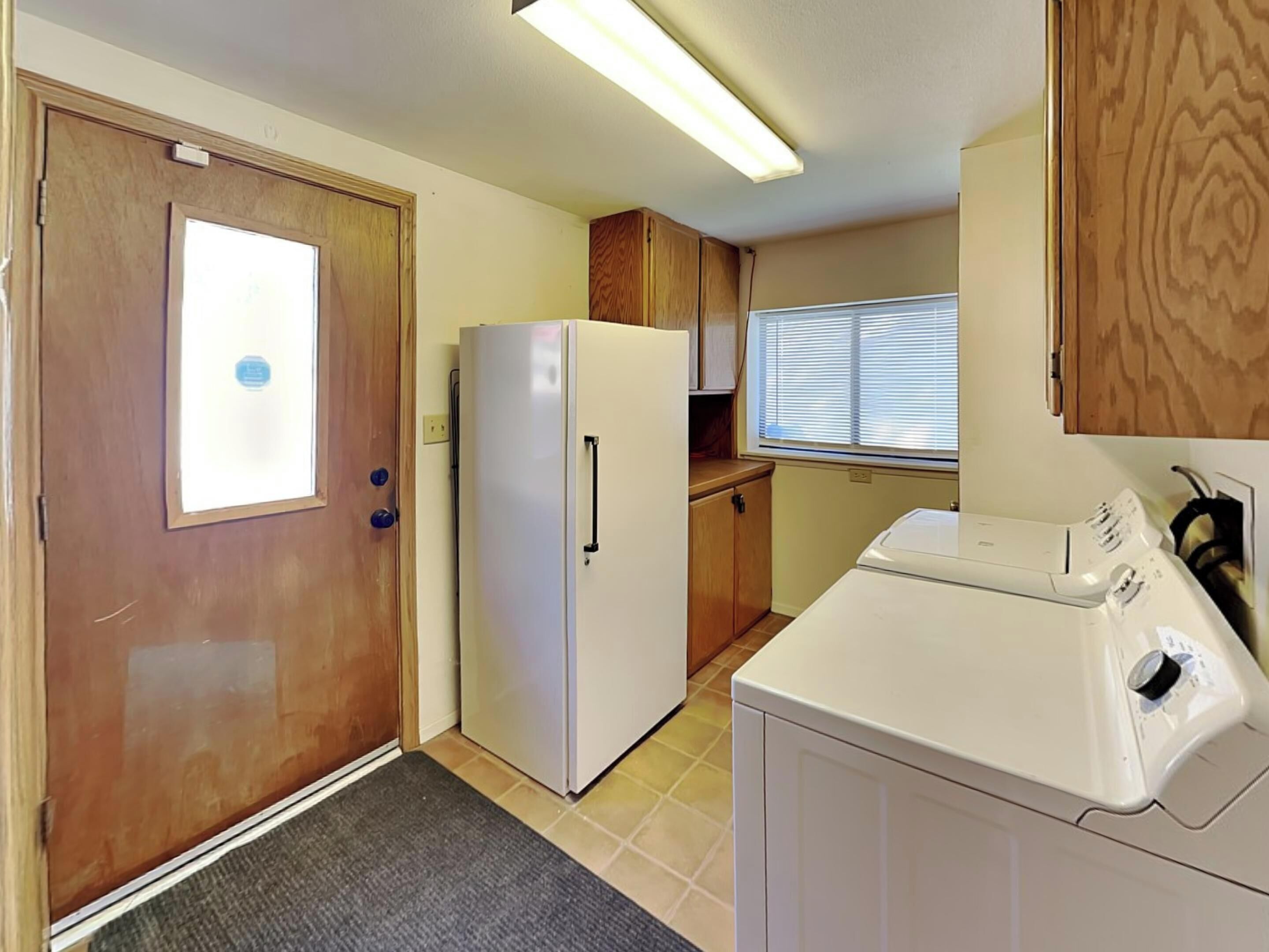 A compact kitchen with a refrigerator, a washing machine, and wooden cabinets.