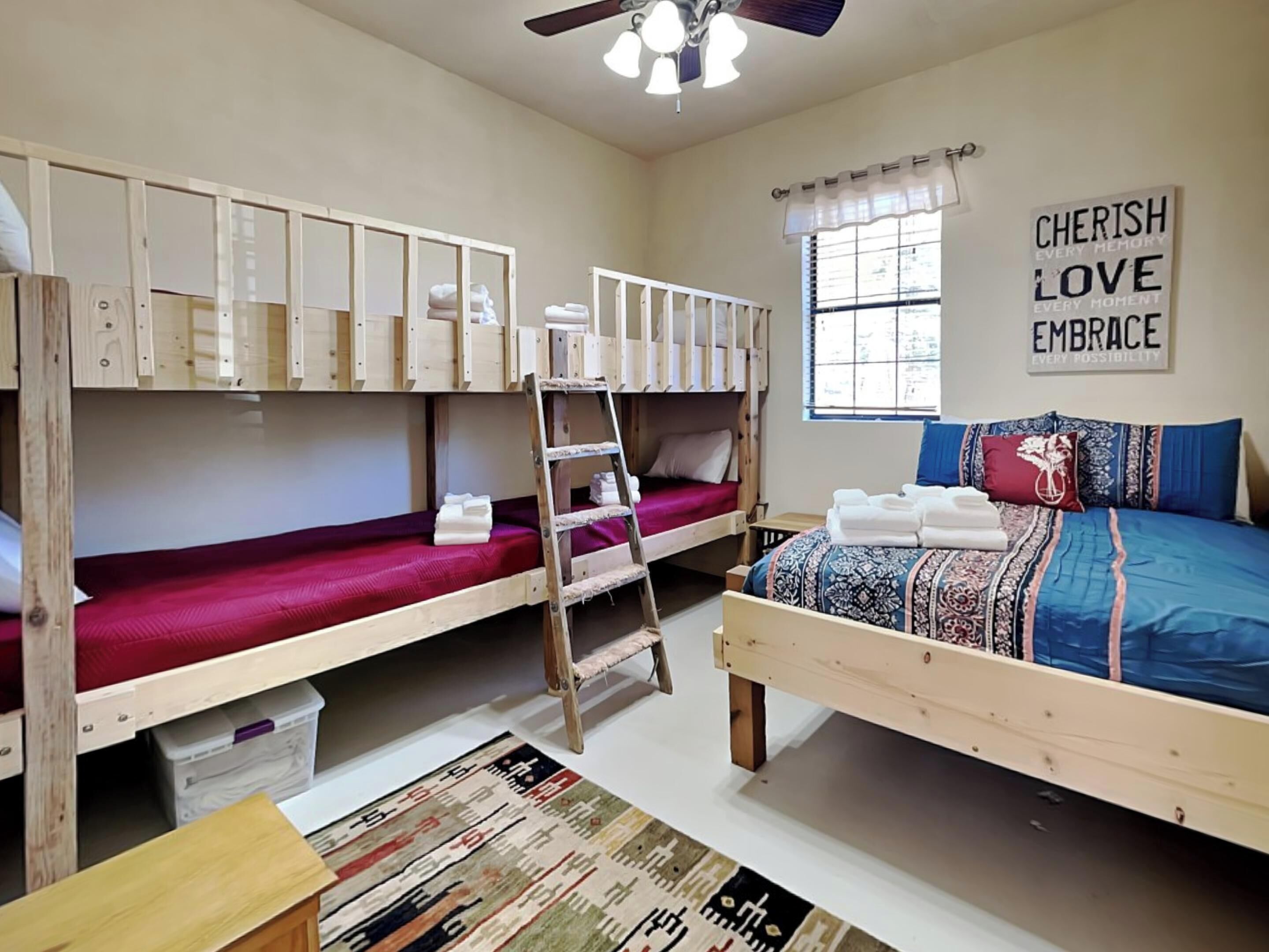 A dormitory room with bunk beds, a ladder, a window with curtains, and a motivational quote on the wall.