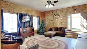 A living room with a sectional sofa, a TV, a Christmas tree, and a large window. - Quiet Mountain Hideaway by Ruidoso Vacation Rentals (Ruidoso)