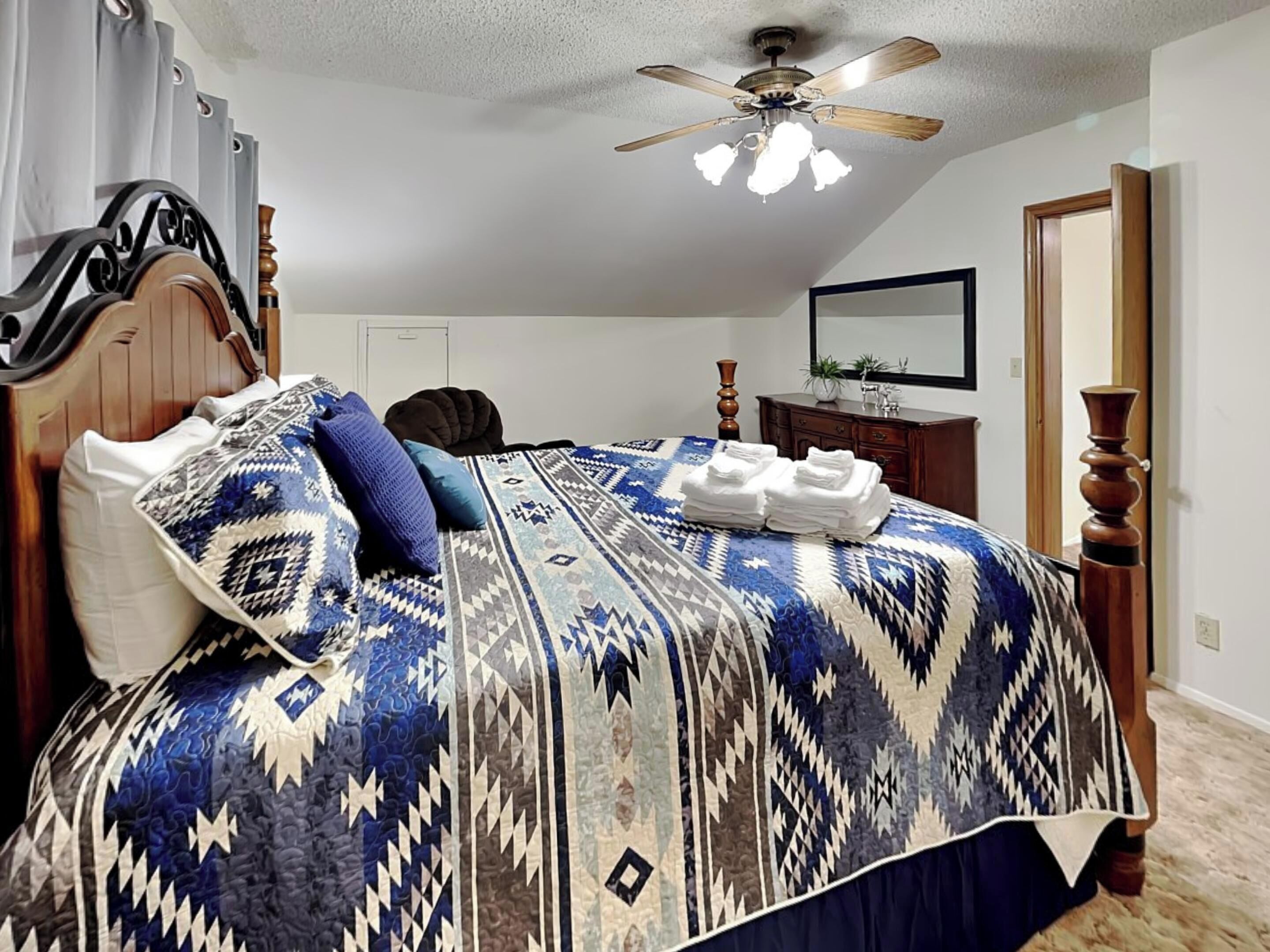 A bedroom with a bed, a ceiling fan, a dresser, and a mirror.