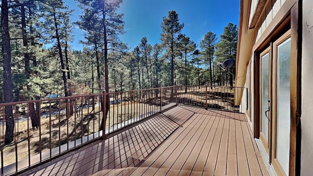 A wooden deck with a metal railing overlooking a forested area. - Quiet Mountain Hideaway by Ruidoso Vacation Rentals (Ruidoso)