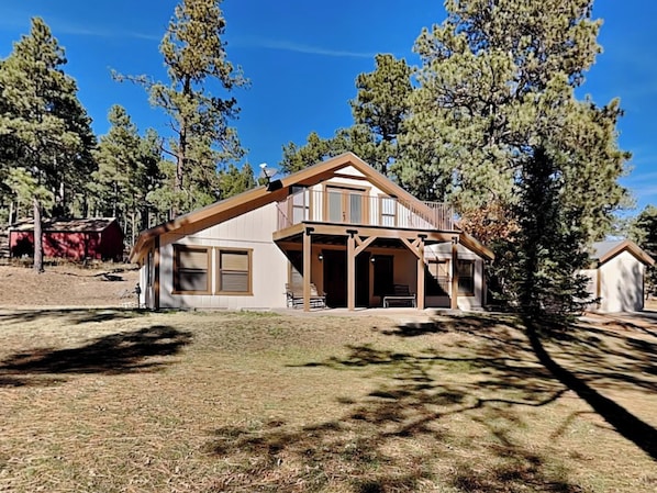 A two-story house with a porch, surrounded by trees.