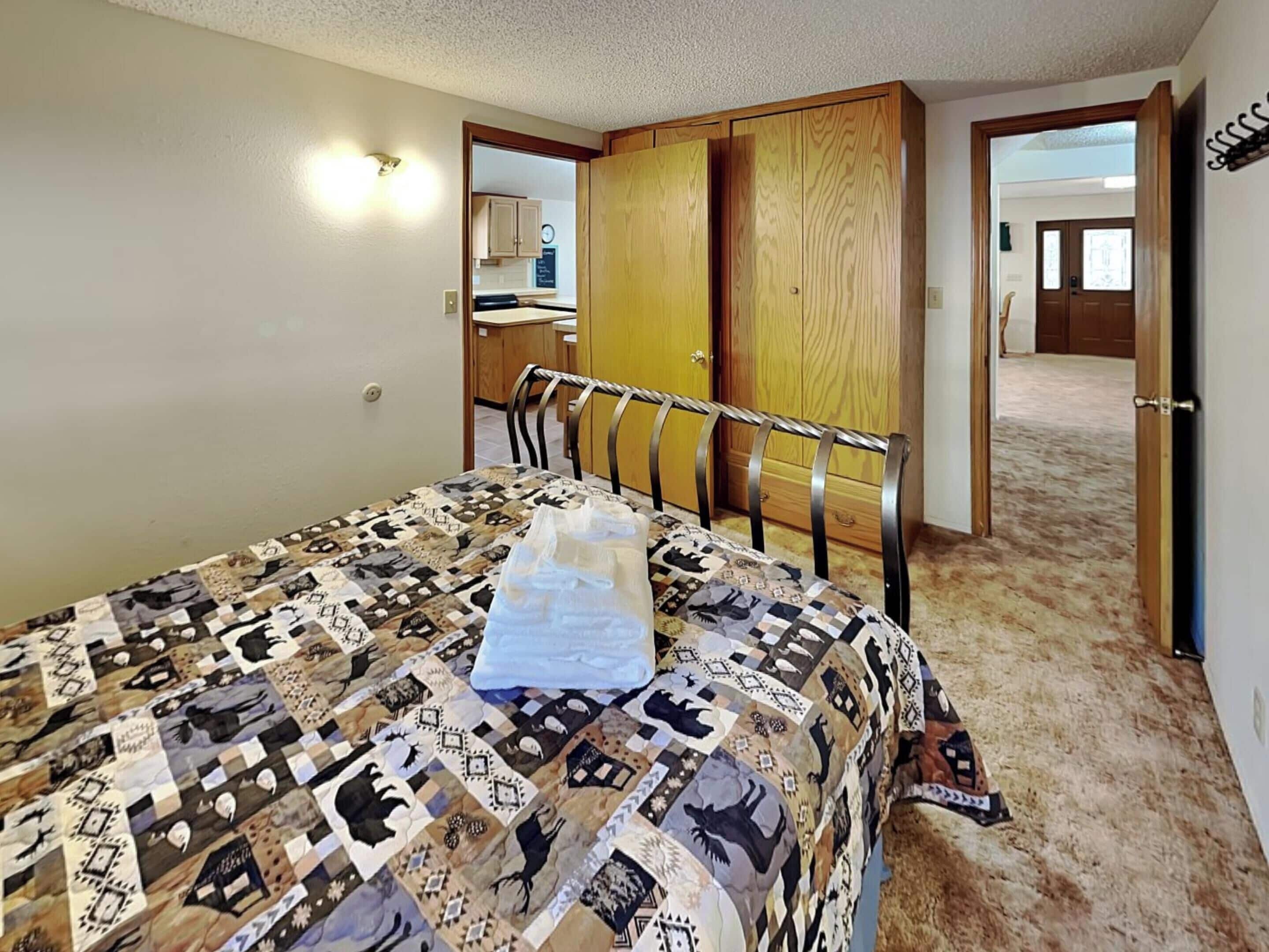 A bedroom with a quilted bedspread, a chair, and a wardrobe.
