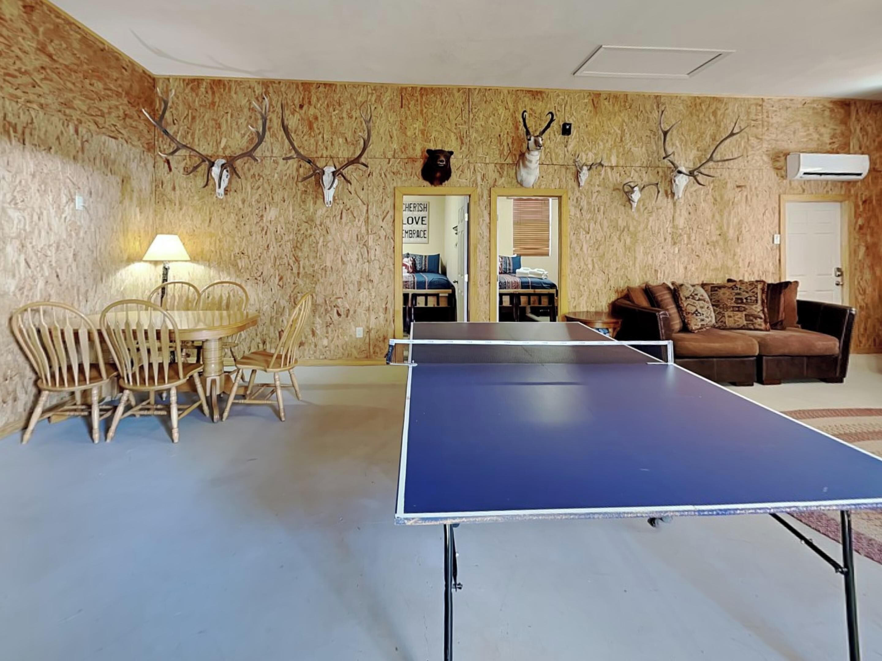 Une pièce comprenant une table de ping-pong, une table à manger avec des chaises, un canapé et des murs décorés de têtes d’animaux empaillées.