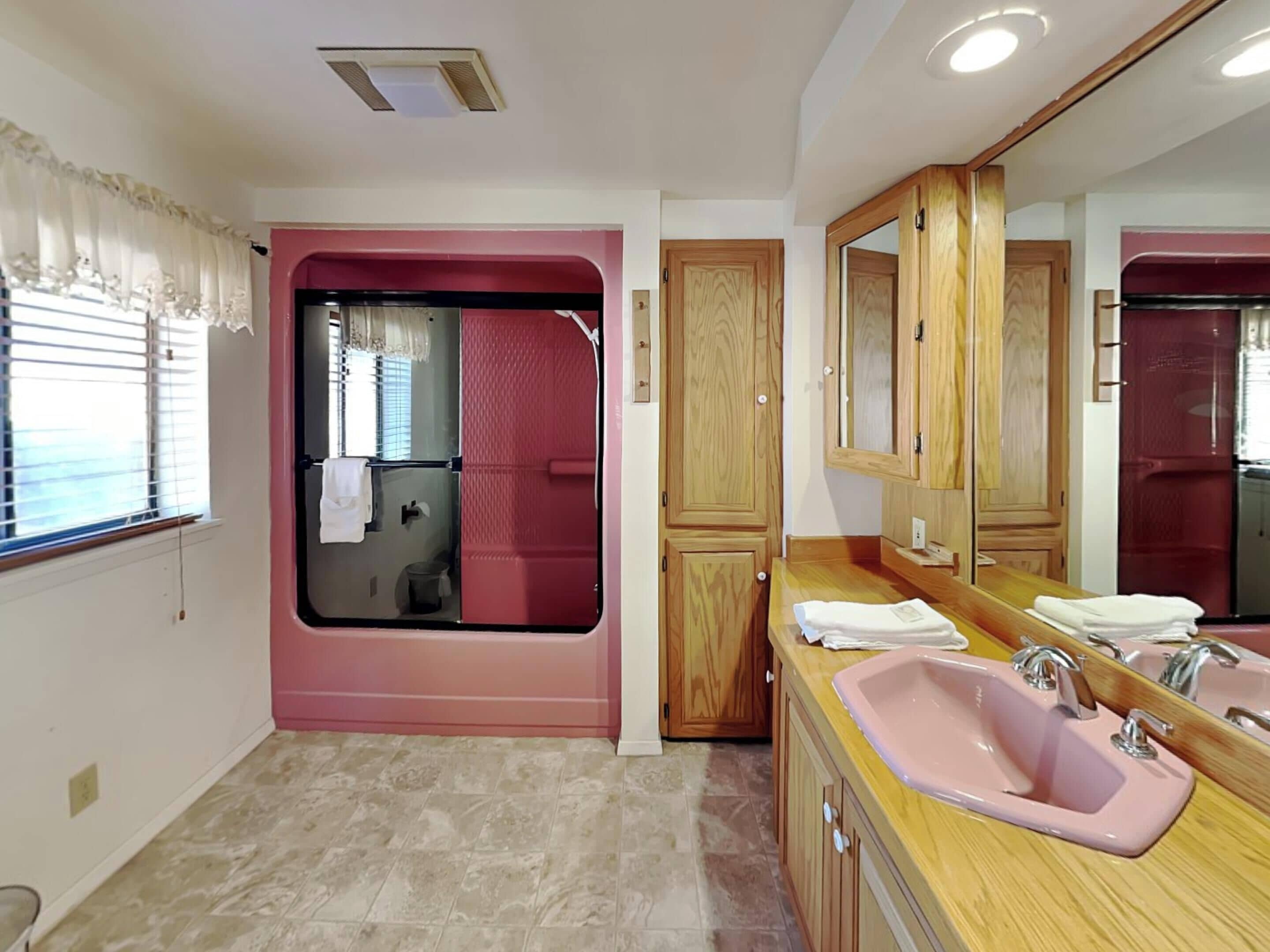 Une salle de bain avec un meuble-lavabo rose, un évier, un miroir et un espace douche.