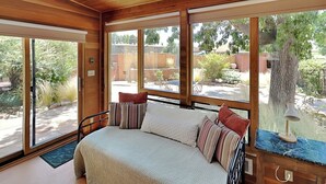 A bedroom with a large bed, wooden ceiling, and multiple windows offering a view of the backyard. - Casa Amarilla by Kokopelli Property Management (Santa Fe)