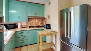 A kitchen with teal cabinets, a stainless steel refrigerator, a wooden table, and a tiled backsplash. - Casa Amarilla by Kokopelli Property Management (Santa Fe)