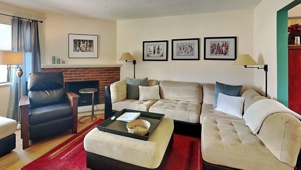 A living room with a sofa, armchair, and ottoman, a fireplace, framed pictures on the wall, and a lamp. - Casa Amarilla by Kokopelli Property Management (Santa Fe)