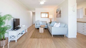 A living room with a TV, sofa, coffee table, and a plant. - Poppy's Place - Oceanstays (Yamba)