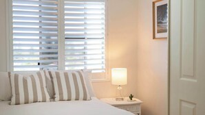 A bed with striped pillows, a bedside lamp, and a framed picture on the wall. - Poppy's Place - Oceanstays (Yamba)