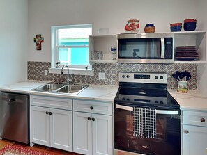 A modern kitchen with white cabinetry, a stainless steel sink, a microwave, an oven, and a window above the sink.