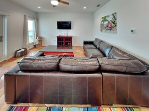 A living room with a brown leather sectional sofa, a flat-screen TV mounted on the wall, and a painting of a car on the wall. - Marlin Manor by Silver Sands Vacation Rentals (Port Aransas)