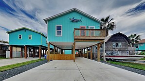 A two-story building with a balcony, a boat docked outside, and a clear sky. - Marlin Manor by Silver Sands Vacation Rentals (Port Aransas)
