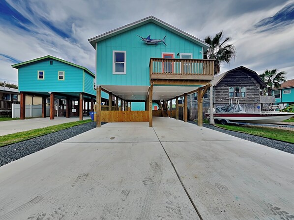 A two-story building with a balcony, a boat docked outside, and a clear sky. - Marlin Manor by Silver Sands Vacation Rentals (Port Aransas)