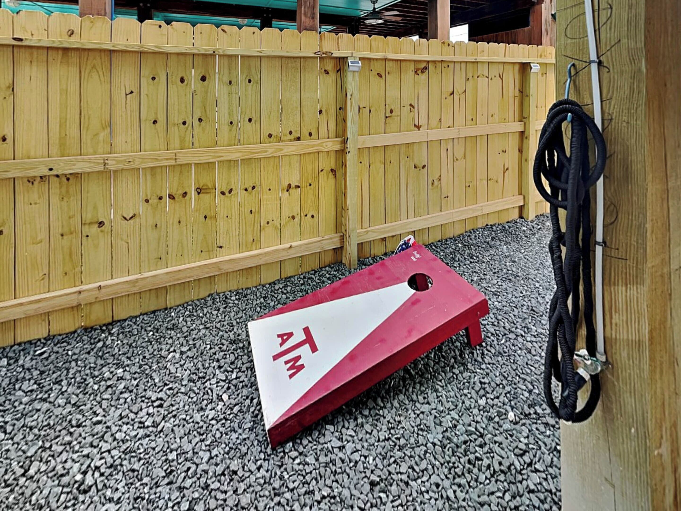 A wooden fence and a red and white board game in a gravel area.