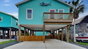 A two-story house with a balcony, a wooden deck, and a boat in the background. - Marlin Manor by Silver Sands Vacation Rentals (Port Aransas)
