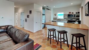 A modern kitchen with a central island, bar stools, and a leather sofa in a living area. - Marlin Manor by Silver Sands Vacation Rentals (Port Aransas)