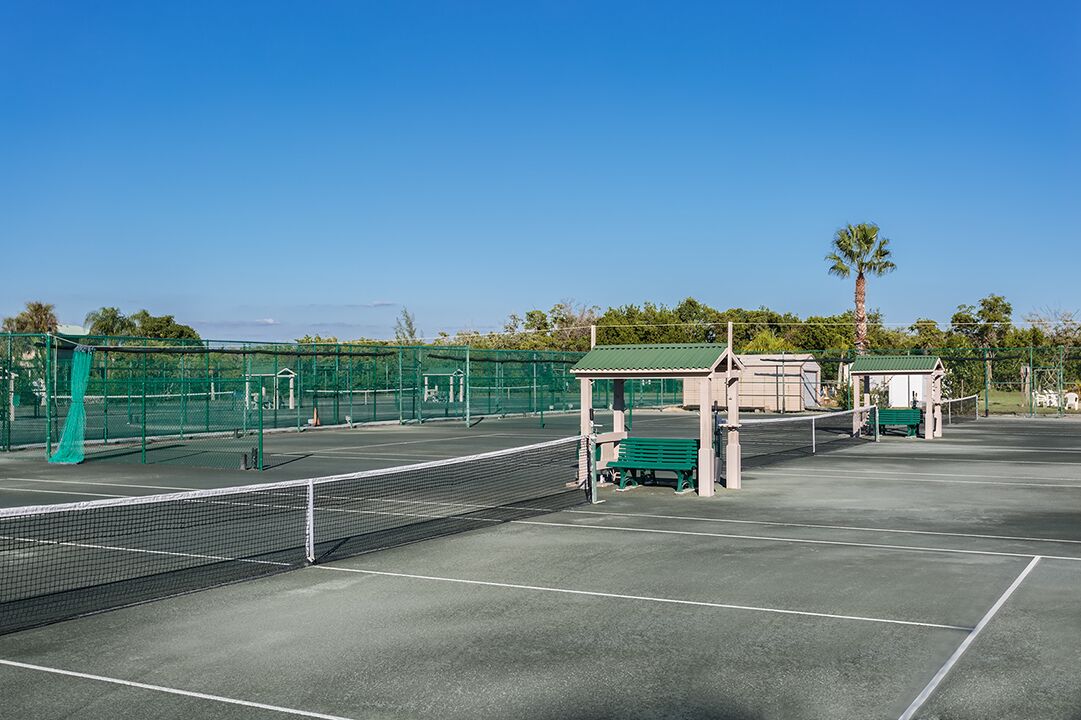 Een tennisbaan met een net, een groen zitgedeelte en een klein paviljoen.