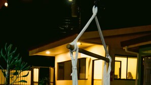 A hammock hanging outdoors at night, with a building in the background. - Habitat Surf Glamp (Cóbano)