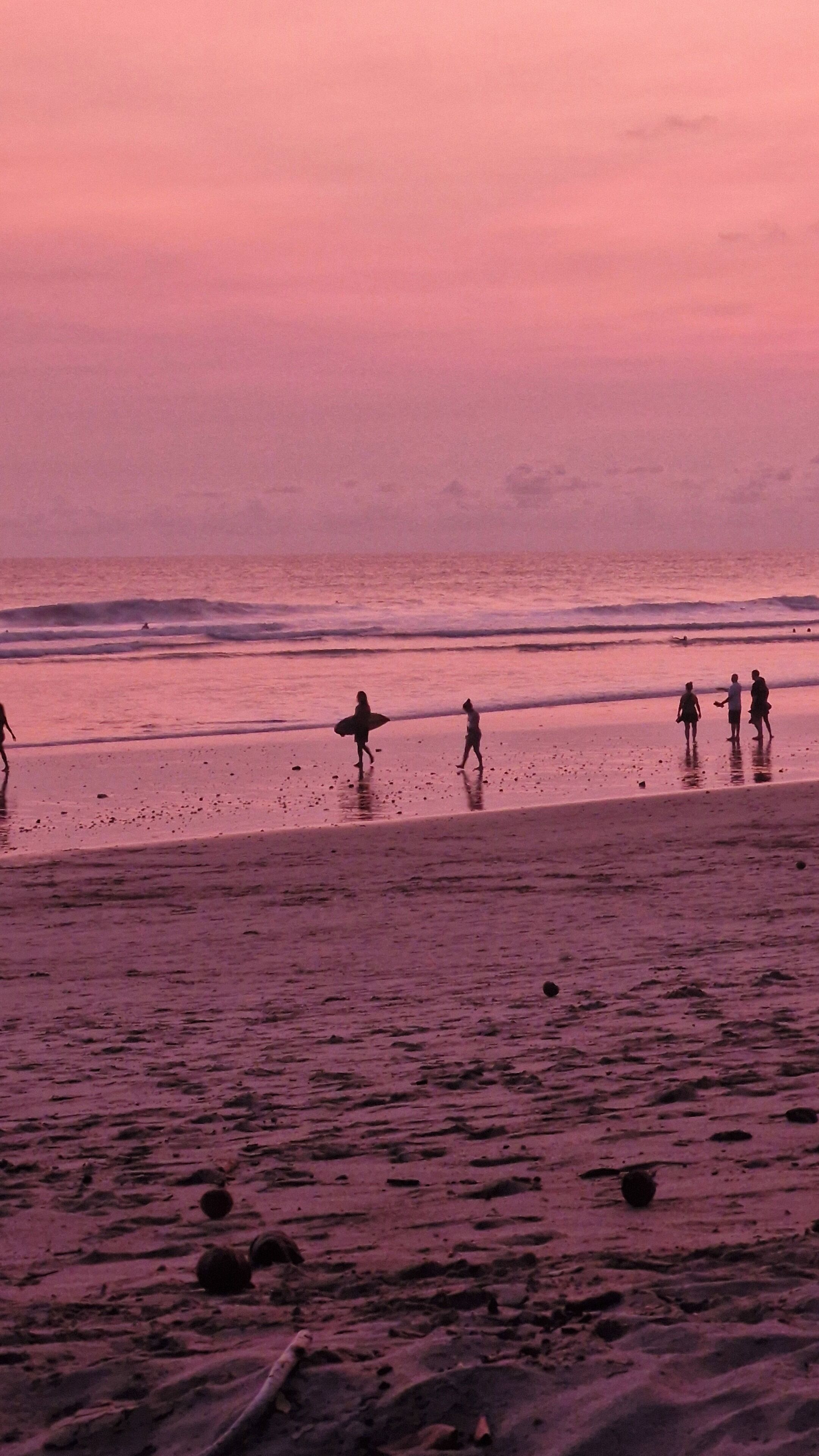 A beach scene with people walking and carrying surfboards.