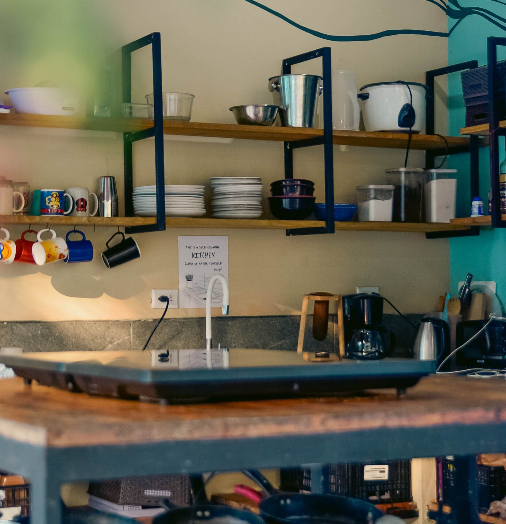 A kitchen with shelves holding plates, bowls, and mugs. There is a sign that says "This is a self-cleaning kitchen."