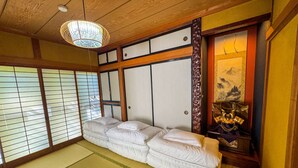 Ett traditionellt japanskt rum med tatamimattor på golvet, en låg säng med vita sängkläder, skjutbara shojidörrar och en hängande lampa.