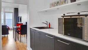 Een moderne keuken met een inbouwoven, een spoelbak en een eethoek met een rode stoel en een televisie.