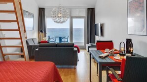 Een moderne hotelkamer met een balkon, een zithoek en een groot raam met uitzicht op zee.