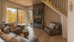 Een moderne woonkamer met een open haard, leren banken en een houten trap.