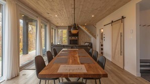 Een ruime eethoek met een lange houten tafel, zwarte stoelen en uitzicht op de omgeving door grote ramen.