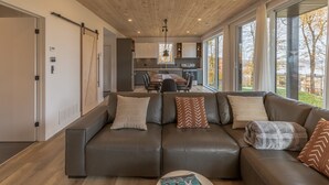 Een moderne woonkamer met een leren bank, een eethoek en grote ramen met uitzicht op de omgeving.