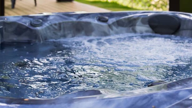 Een hottub met uitzicht op een houten terras en bomen.