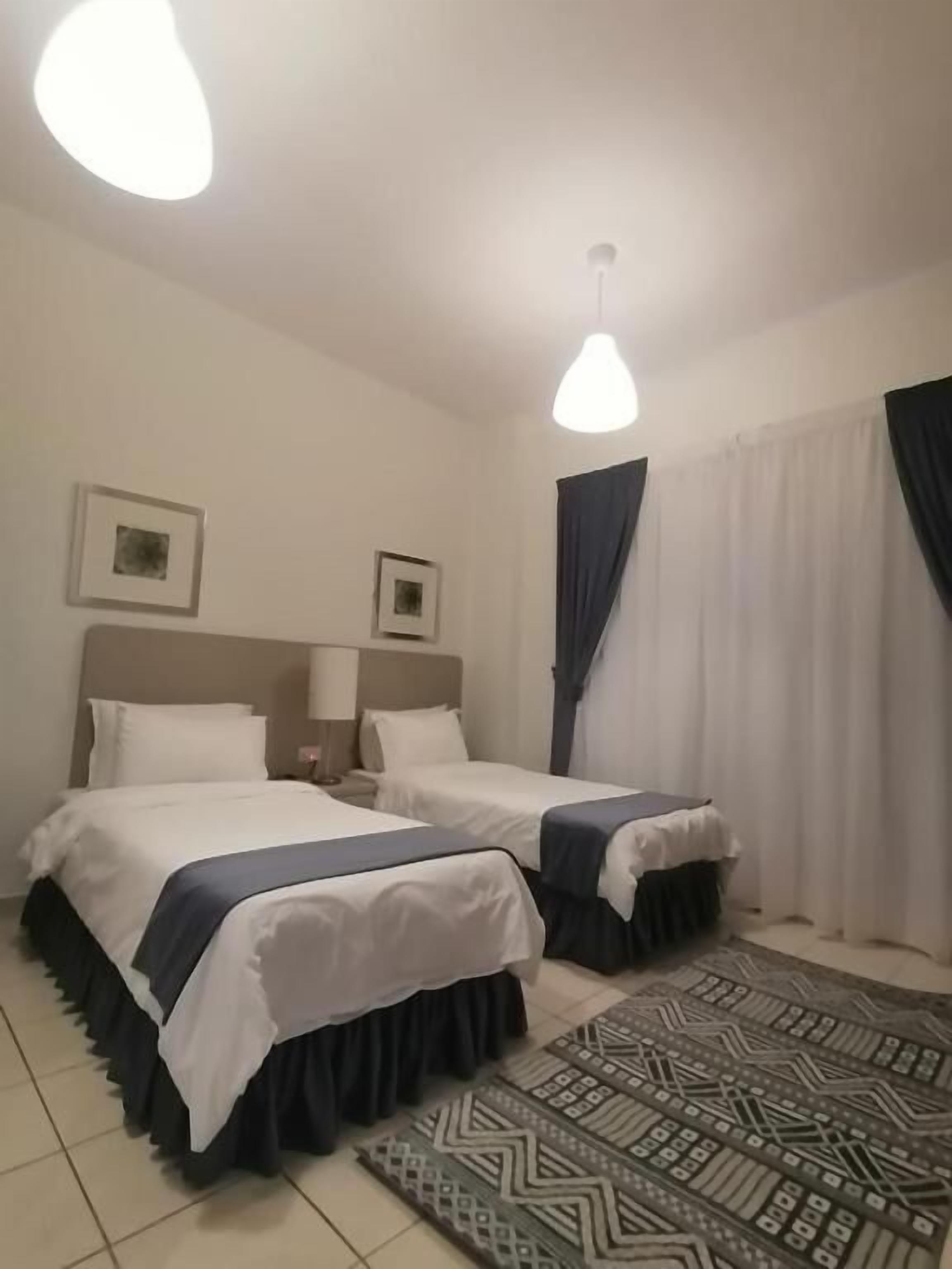 Ein Hotelzimmer mit zwei Betten, einem gemusterten Teppich und einem großen Fenster mit Vorhängen.