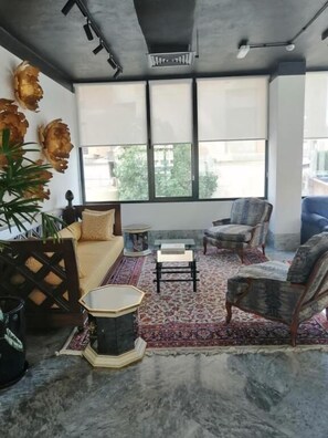 A room with a sofa, armchairs, a coffee table, a patterned rug, and a large window with blinds.