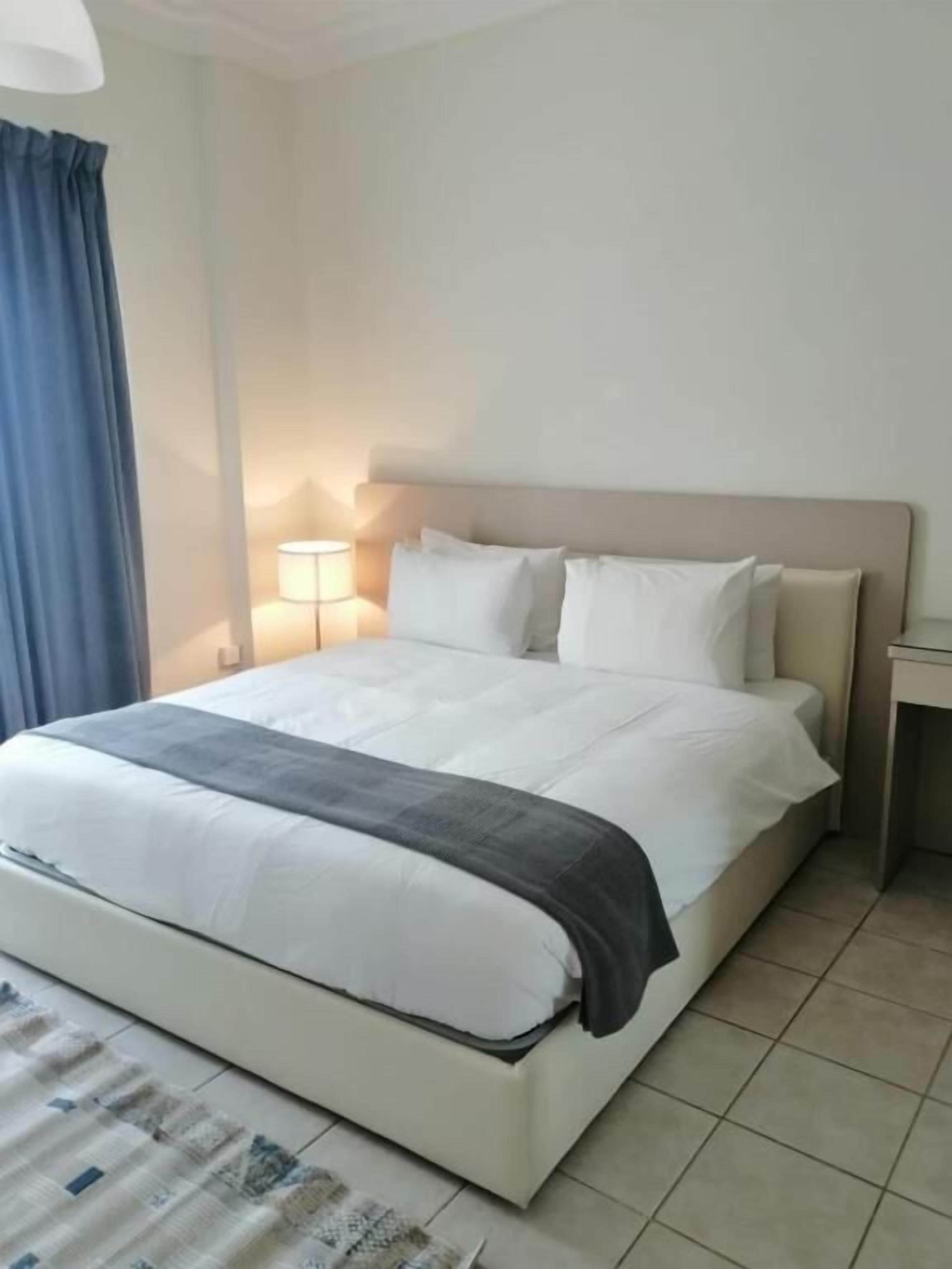 A hotel room with a bed, a bedside table, a lamp, and a window with curtains.