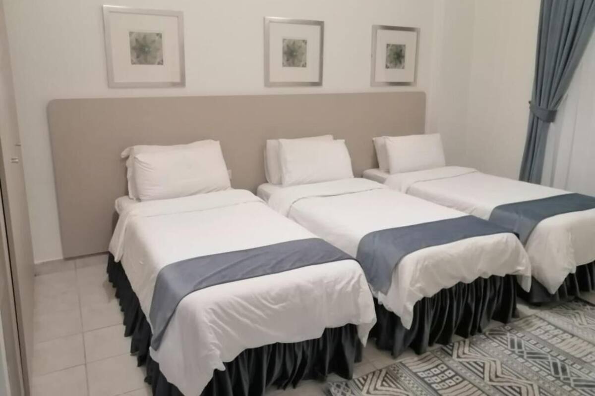 Una habitación de hotel con cuatro camas individuales, un cabecero grande y una alfombra estampada.