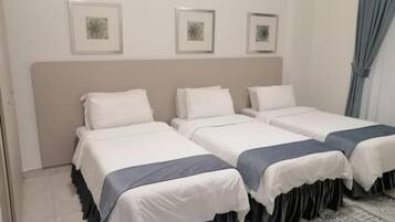 A hotel room with four single beds, a large headboard, and a patterned rug.