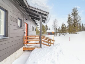 Une cabane en bois dotée d’un porche abrité et surplombant un paysage enneigé.
