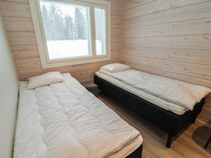 Eine kleine, einräumige Holzhütte mit zwei Betten und einem Fenster mit Jalousien.