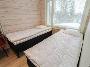 Une chambre avec deux lits, une fenêtre avec des stores et un mur en bois.