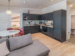 Une cuisine compacte dotée d’appareils électroménagers modernes, un coin repas avec une table ronde et des chaises rouges, et un canapé gris.
