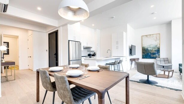 Una cocina moderna con armarios blancos, horno empotrado y comedor con mesa y sillas de madera.