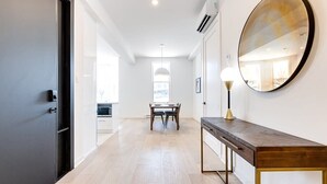 Un pasillo moderno con una mesa y sillas de madera, un espejo redondo y una lámpara.