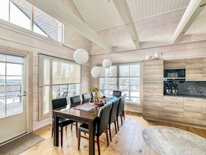 Un vaste espace dédié à la salle à manger, avec une table et des chaises en bois, de grandes fenêtres et une vue sur l’extérieur.