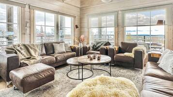 A spacious living room with leather sofas, a round coffee table, and large windows offering a view of the outdoors.