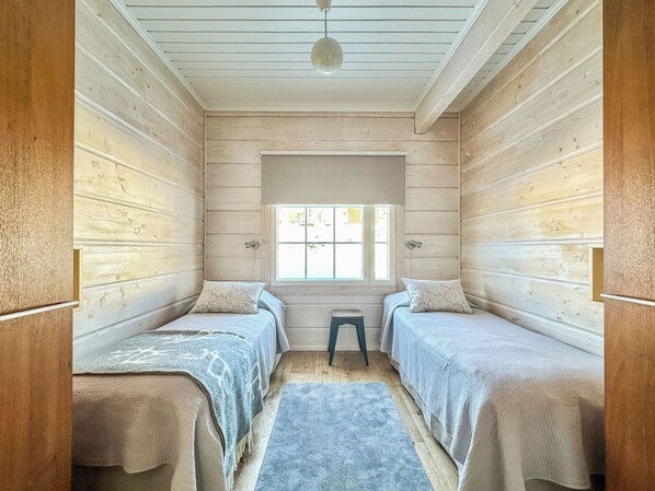 Una habitación con dos camas, un taburete pequeño y una ventana.