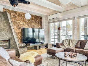 Una sala de estar moderna con pared de piedra, televisor de pantalla plana, sofás de cuero, una mesa de centro redonda y ventanas amplias.